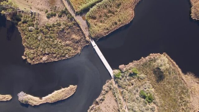 Birds-eye view of a wooden bridge over the dark water of &Eacute;tang de Foce as it flows towards the beach at Ostriconi in the Balagne region of Corsica