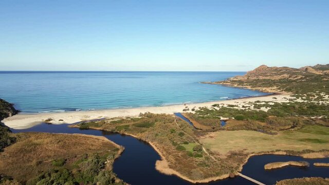 Aerial view of the Etang de Foce as it flows to the white sandy beach of Ostriconi in the Balagne region of Corsica with the Desert des Agriates in the distance