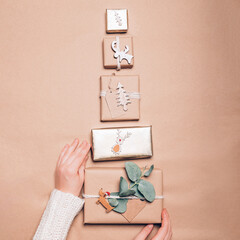 Hands are holding Xmas tree tower made from Gifts wrapped in recycled brown paper with handmade toppers, christmas background with minimalist style wrapping, top view flat lay