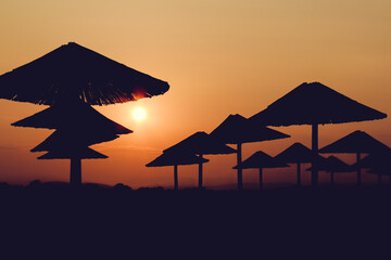 Fototapeta na wymiar The sunset red sun illuminates the beach silhouette straw umbrellas