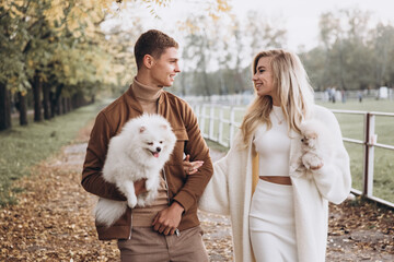 Beautiful young couple in autumn walks with dogs, pomeranian, in the park