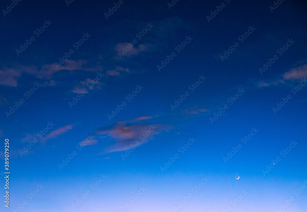 Wall mural blue sky at twilight with sparse pink clouds and crescent moon rising