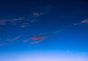 Blue sky at twilight with sparse pink clouds and crescent moon rising