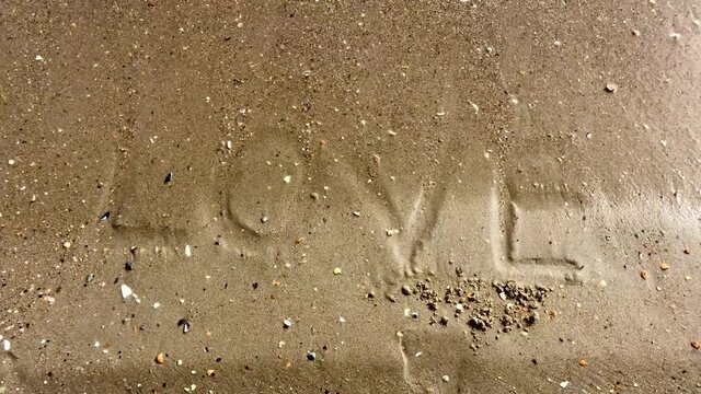 Sea waves gradually wash away the inscription "Love" on the sandy beach