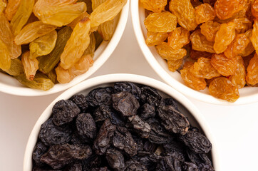 Two types of yellow and black raisins in a white plate on a white background