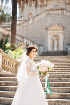 beautiful bride in tender wedding dress with bridal bouquet on the stairs of the Nativity of the Blessed Virgin Mary church in Prcanj