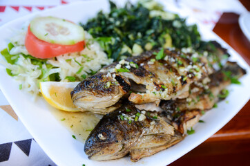Grilled trout on plate on a table in restaurant. Tasty fresh fish served with potato and spinach....
