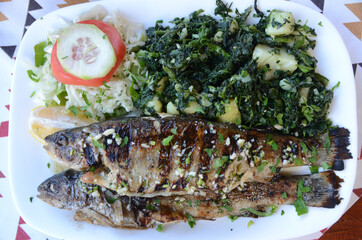 Grilled trout on plate on a table in restaurant. Tasty fresh fish served with potato and spinach....