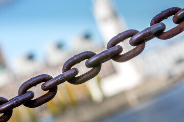 Une chaîne traverse l'image du bas à gauche vers le haut à droite. À l'arrière-plan, un immeuble très flou.