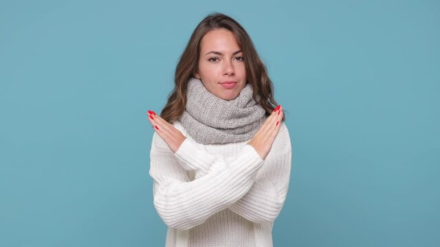 Displeased young woman in sweater scarf isolated on blue background studio. Healthy lifestyle ill sick treatment cold season concept. Looking camera showing stop gesture with palm crossed hands say no