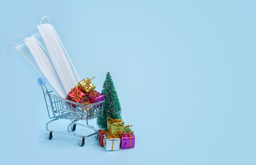 Gift boxes, christmas tree, medical mask, shopping trolley on blue background.The concept of safe online shopping during quarantine and the spread of coronavirus. Copy space fot text.
