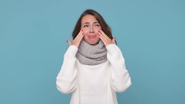 Angry crying displeased young brunette woman in sweater scarf posing isolated on blue background studio. Healthy lifestyle ill sick treatment cold season concept. Spreading hands screaming ask why