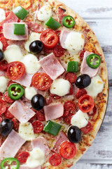 Pizza with ham, mozzarella cheese, cherry tomatoes, green and jalapeno pepper, black olives and fresh basil. Bright background. Top view. Close up. 