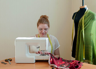 tailor working near sewing machine with red vest on wooden table in studio