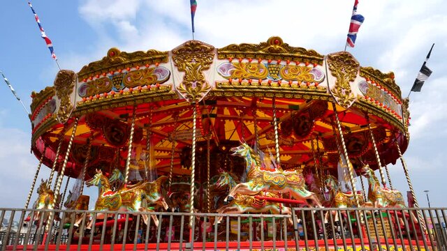 Colorful carousel merry-go-round roundabout with social distancing screens fitted is spinning. Low angle shot against white clouds in the blue sky.