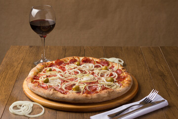 Pepperoni sausage pizza with slices of onions and green olives. Glass of Red Wine to accompany the meal. Typical Brazilian food from Italy. Similar to Pepperonie's pizza.