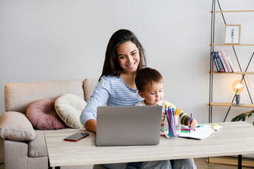 Young beautiful woman multitasking, working from home & teaching two year old son to draw. Woman...