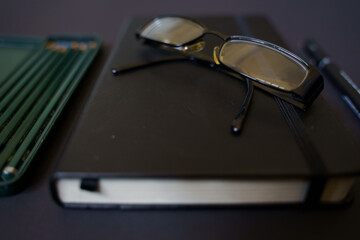 Notebook, pen and glasses on a black background