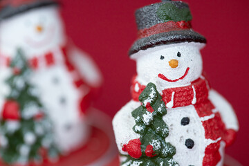 Smiling Christmas snowman with a Christmas tree in his hand. Christmas decoration on a red background.