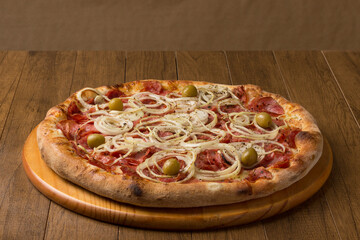 Photo of a pepperoni pizza, slices of onions, mozzarella cheese and green olives. On a wooden board. Horizontal photography.