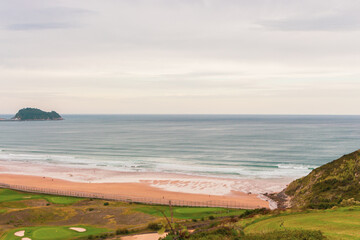 Aerial view of golf field and coast of Bay of Biscay, Basque country. Scenic surf beach and golf field, top view. Panoramic landscape with sea shore and big waves. Scenic seascape with countryside.