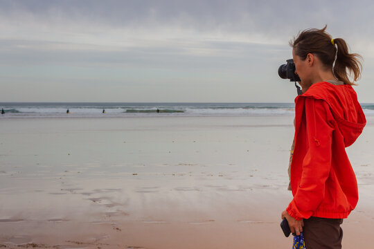 Girl with camera Canon on the scenic autumn beach. Photographer at wide seaside on cloudy day. Tourism and travel concept. Leisure and hobby concept. Woman with camera walking on beach. 