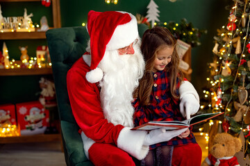 Fototapeta na wymiar Santa Claus with a little cute girl read book in the room. Christmas time.