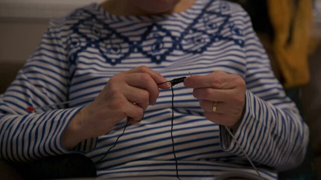 close up of woman knitting with black whool at home to create a doll. focus on knitting needle