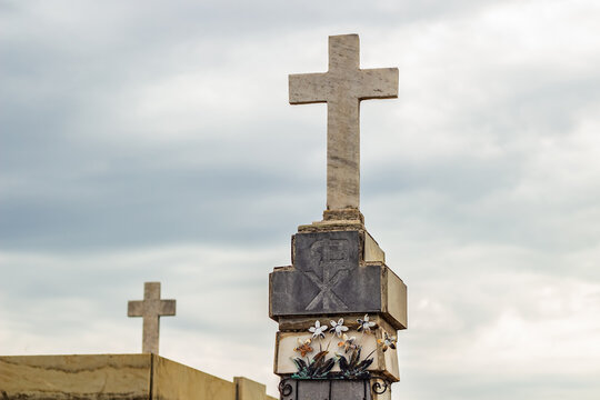 Duas cruzes no topo de mausoléus em cemitério com céu azul com algumas nuvens ao fundo.
