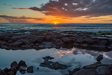 Fototapeta na wymiar Orange sunset over ocean with waves and lava rock beach shoreline