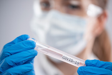 Close-up view of microbiologist in protective glasses, face mask and gloves holds biological tube with covid-19 sample. Backstage of examines coronavirus infection. Healthcare and medical concept.