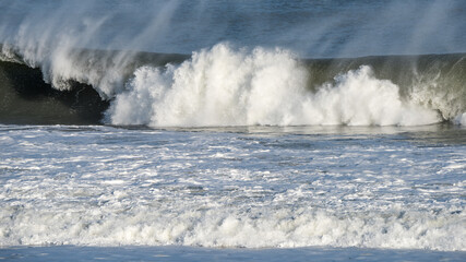Wave breaking with spray and foam at the shoreline on the Atlantic Ocean.