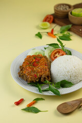 Ayam geprek, Indonesian popular streed food, made from crispy chicken smashed with sambal or chili sauce, eat with rice and cucumber, lettuce, tomato and kemangi. Isolated background, copy space.
