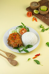 Ayam geprek, Indonesian popular streed food, made from crispy chicken smashed with sambal or chili sauce, eat with rice and cucumber, lettuce, tomato and kemangi. Isolated background, copy space.