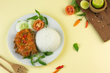 Ayam geprek, Indonesian popular streed food, made from crispy chicken smashed with sambal or chili sauce, eat with rice and cucumber, lettuce, tomato and kemangi. Isolated background, copy space.