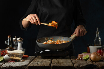 Professional chef stirring curry in pan wok. Backstage of cooking traditional Indian chicken curry on dark blue background. Frozen motion. Concept of cooking tasty hot meal.