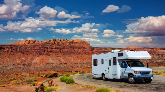 white RV / campervan in canyonlands USA with red cliffs and blue sky and clouds moving behind it