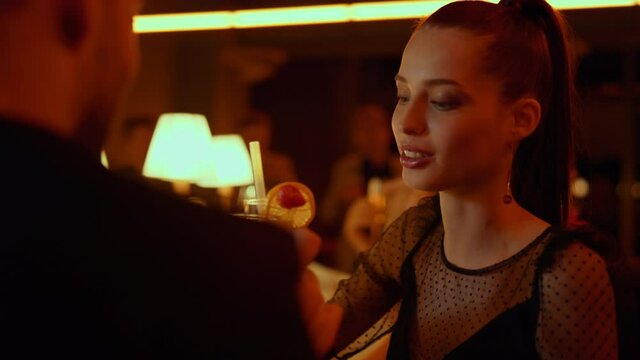Man and smiling woman clinking glasses in bar. Girl drinking cocktail in club