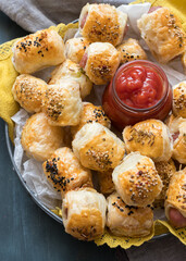 Closeup view of a cooling rack covered with a yellow cloth full of homemade sausage rolls. A jar of...