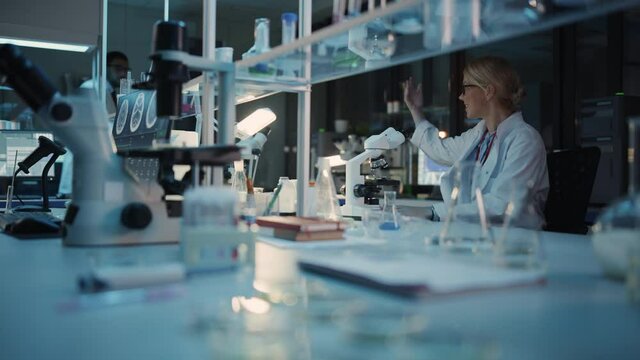 Surprized Female Reseach Scientist Makes an Important Discovery While Researching Virus Vaccine Samples Under the Microscope. She Calls Colleagues and Shares Her Success with Fellow Bioengineers.