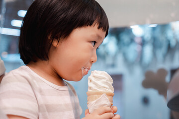 Asian 3 year old girl with  face eat ice cream cone. Concept for  sweet food and family life.