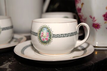 White ceramic cup with decorations. The rest of the tableware in the background.