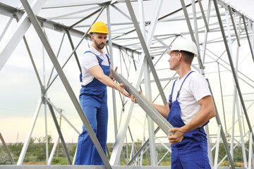 Naklejka na ściany i meble Workers building high voltage tower construction outdoors. Installation of electrical substation