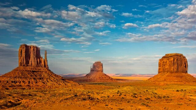 Dramatic western scene at monument valley with white clouds moving against a blue sky and red sandstone structures in the foreground