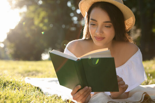 Beautiful young woman reading book in park