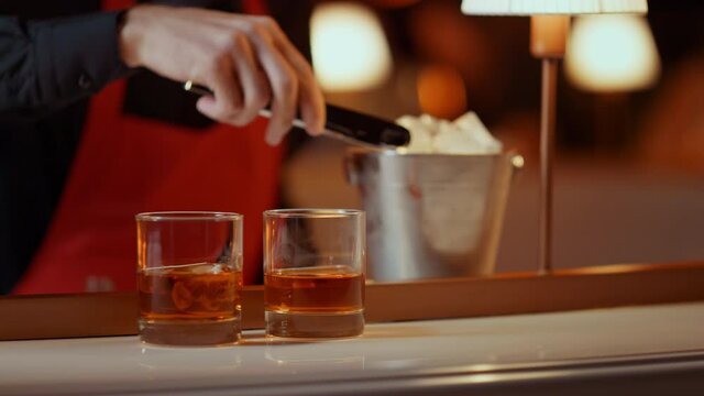 Barman hands preparing whiskey for people in nightclub. Man putting ice cubes