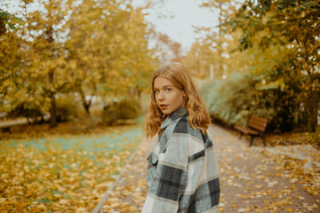 Fototapeta premium The girl walks in the autumn park. Beautiful blonde looks into the camera. Teenager