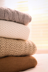 Stack of folded warm sweaters on bed indoors, closeup