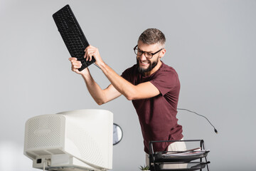 Nervous businessman holding computer keyboard near monitor on blurred foreground in office