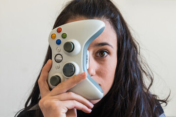 Una chica morena joven sujeta un mando inalámbrico  blanco para jugar a videojuegos